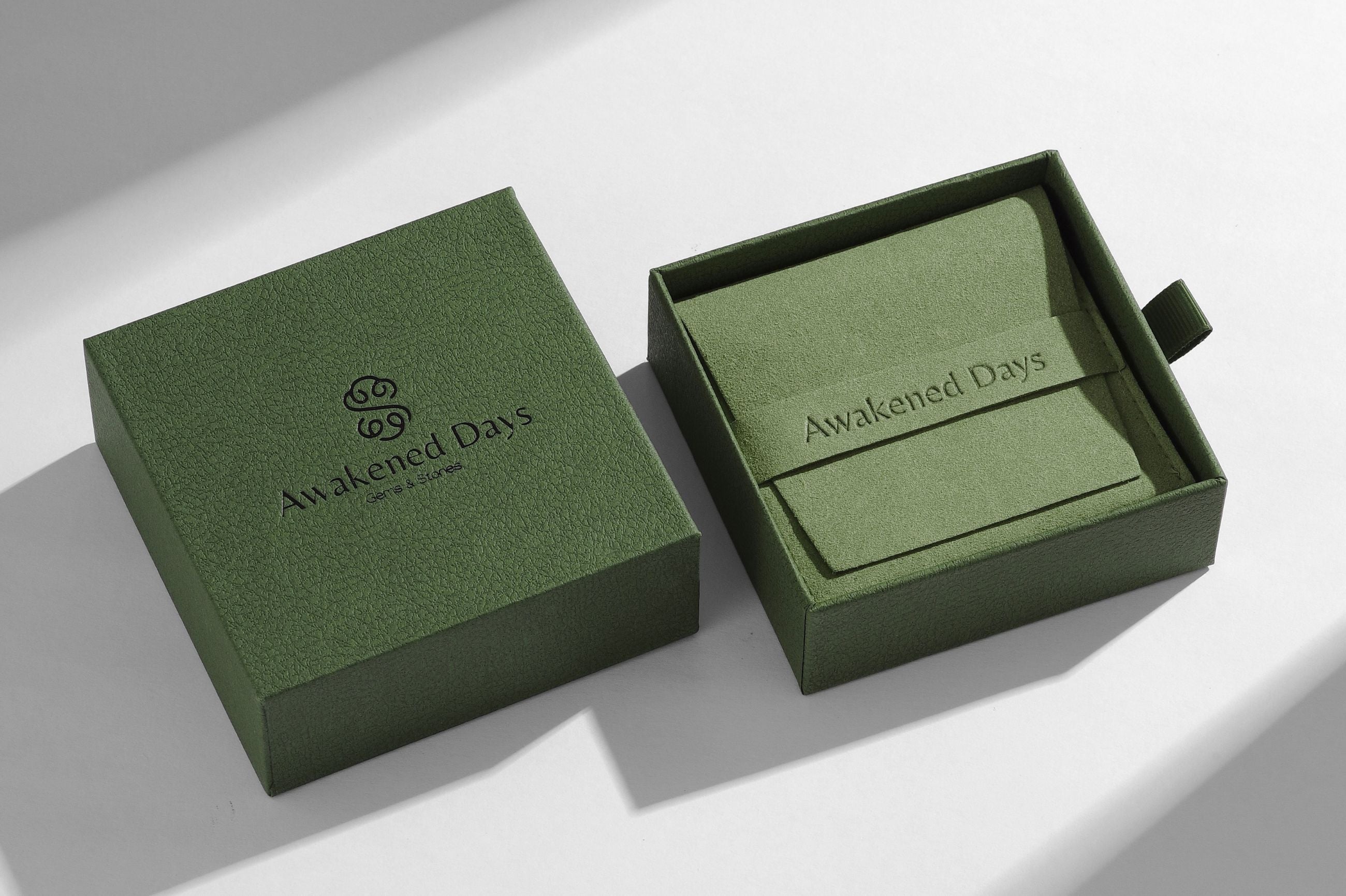 Green 'Awakened Days' branded jewelry box on a light grey background